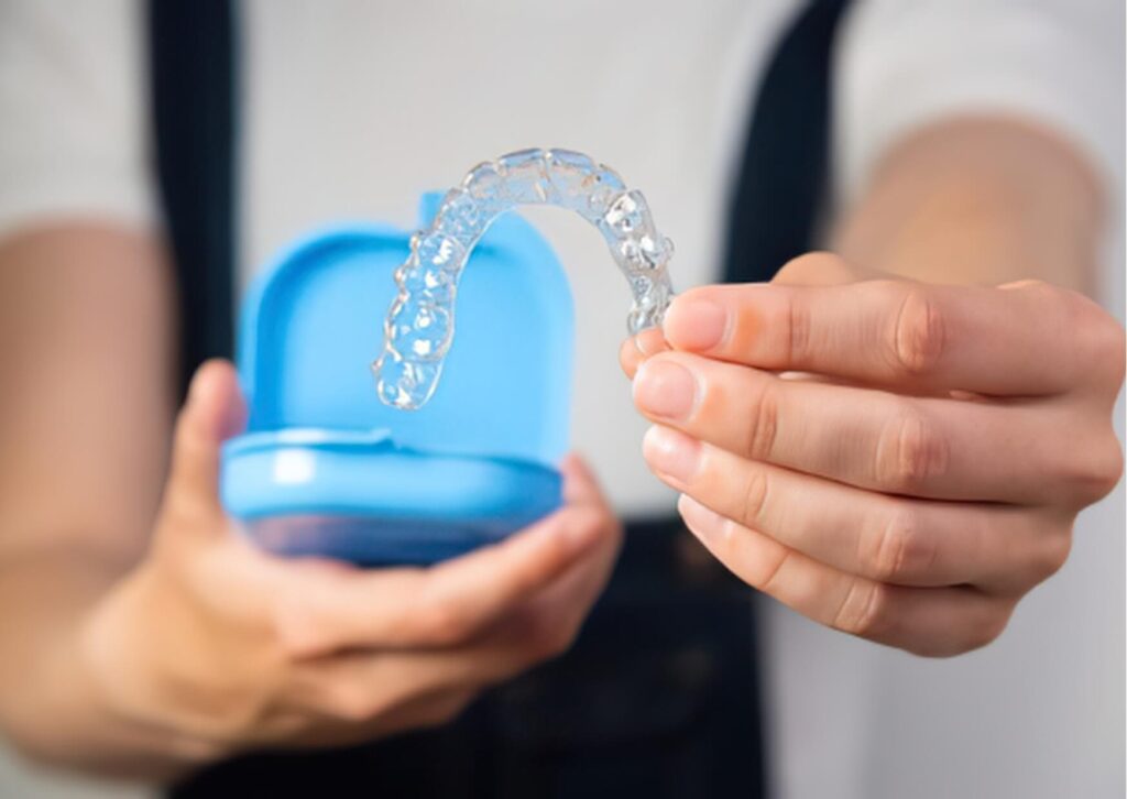 Person holding a custom clear nightguard and storage case before wearing it to protect teeth from grinding during sleep.