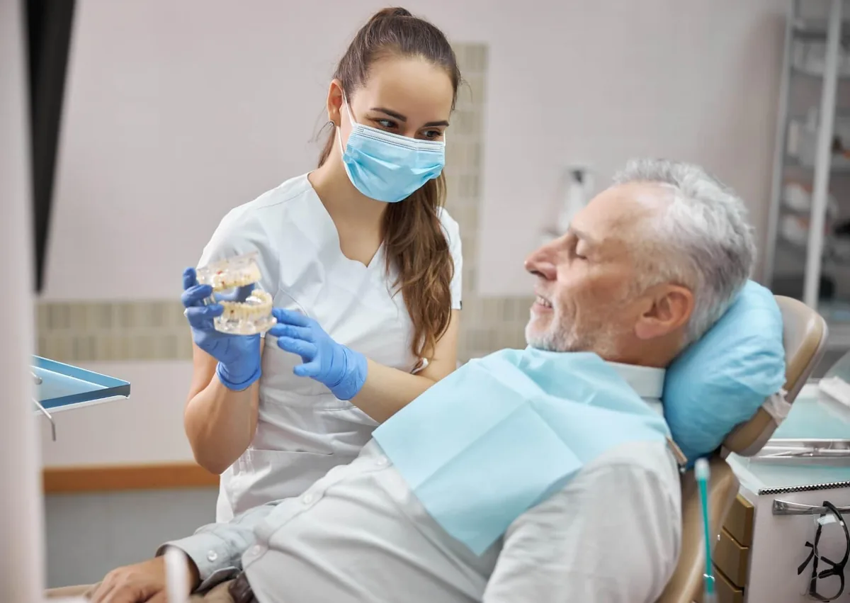 Dental professional showing a patient a model of full mouth dental implants during a consultation.