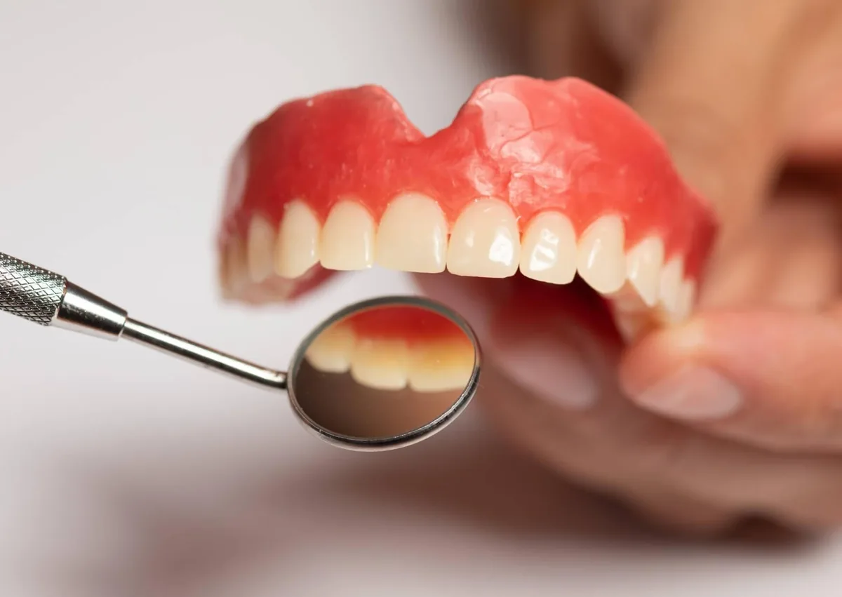 Close-up of dentures being examined with a dental mirror for fit and condition.
