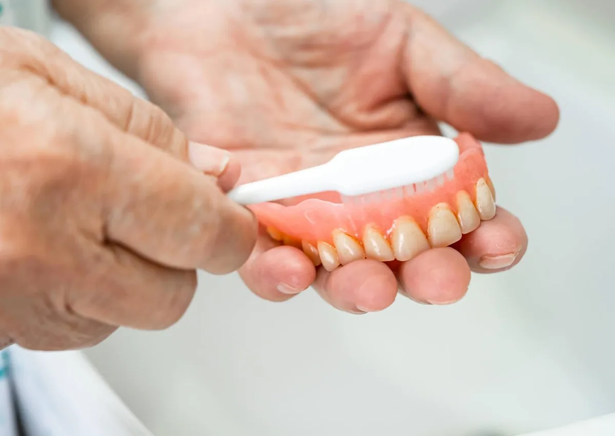 Person brushing dentures to remove food and plaque as part of daily denture care.